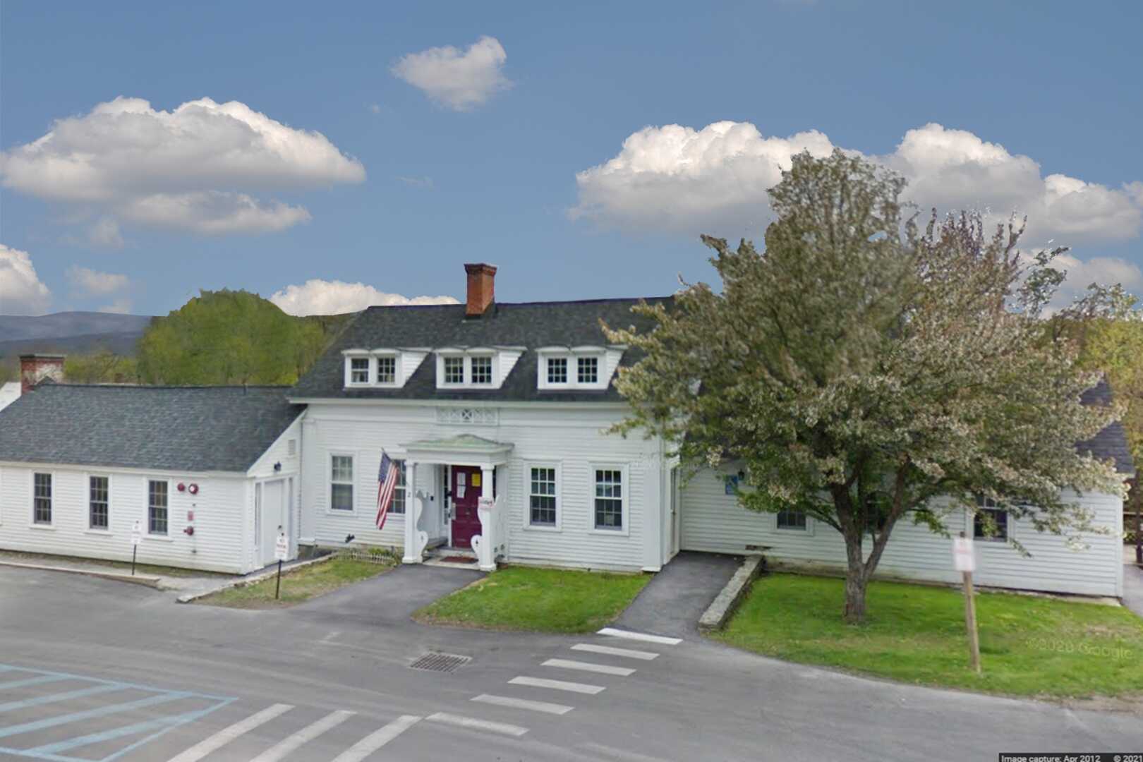 An old white colonial house that has been converted into a business location. There is a beautiful blue sky with clouds and a tree out front.