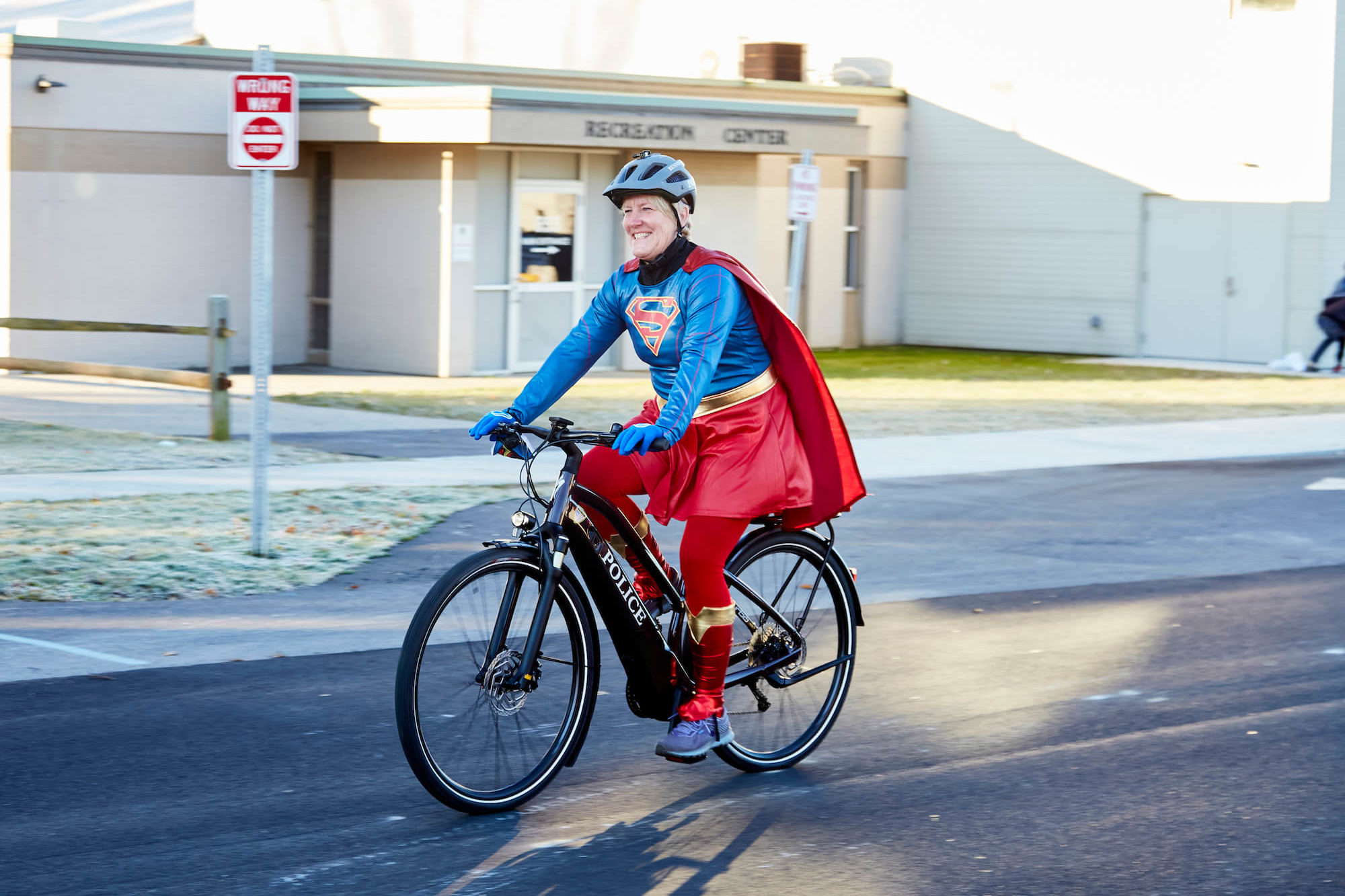 A woman in a superman costume ride an ebike with her cape blowing in the wind.