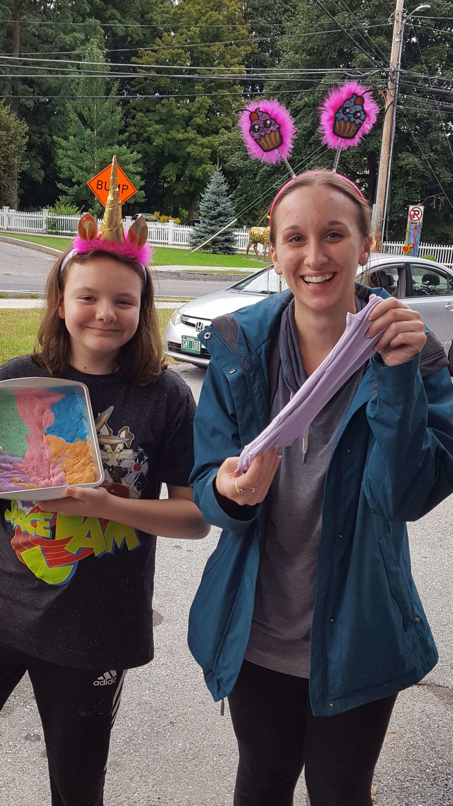 two girls smiling wearing silly head bands. One has a unicorn horn and the other has cupcake ears