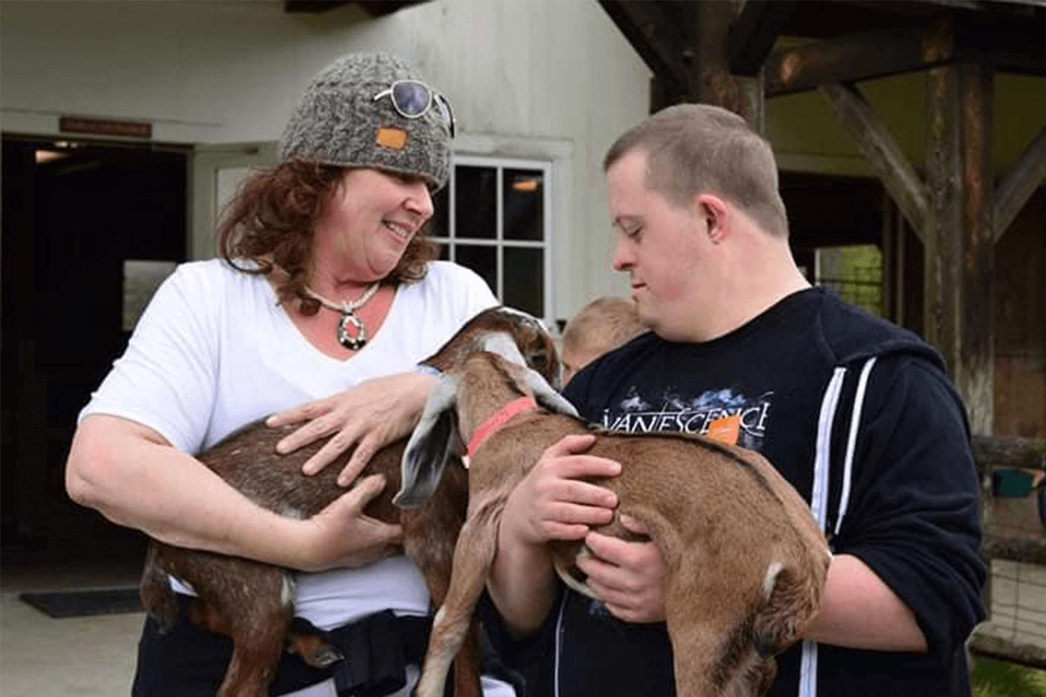 One women and one man holding baby goats outside