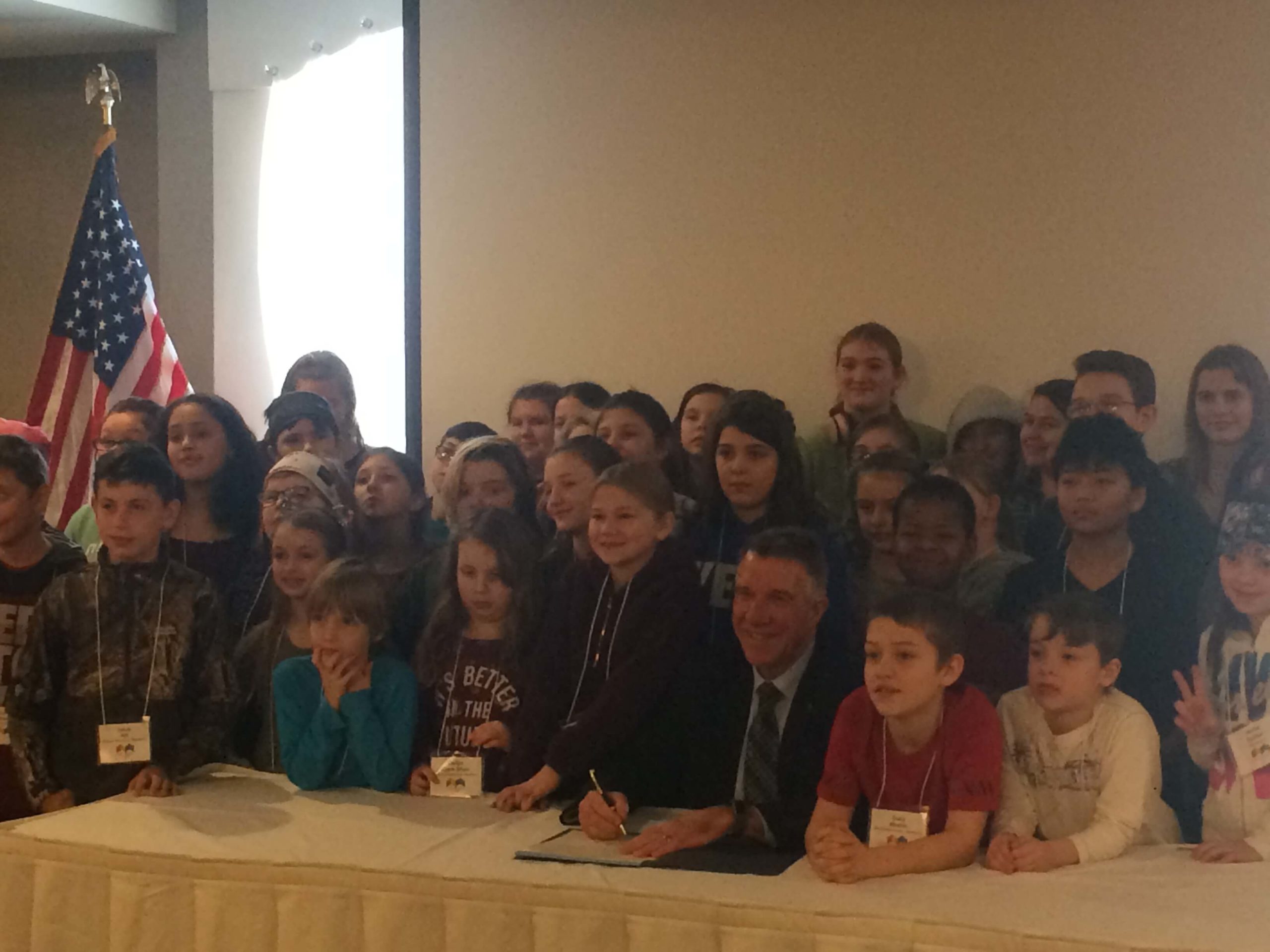 Children posing with Vermont governor Phil Scott as he signs a document