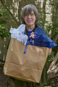 A middle-age woman with short gray hair poses outside with a gift bag