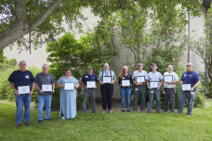 A group of men and women lined up outside holding a framed award